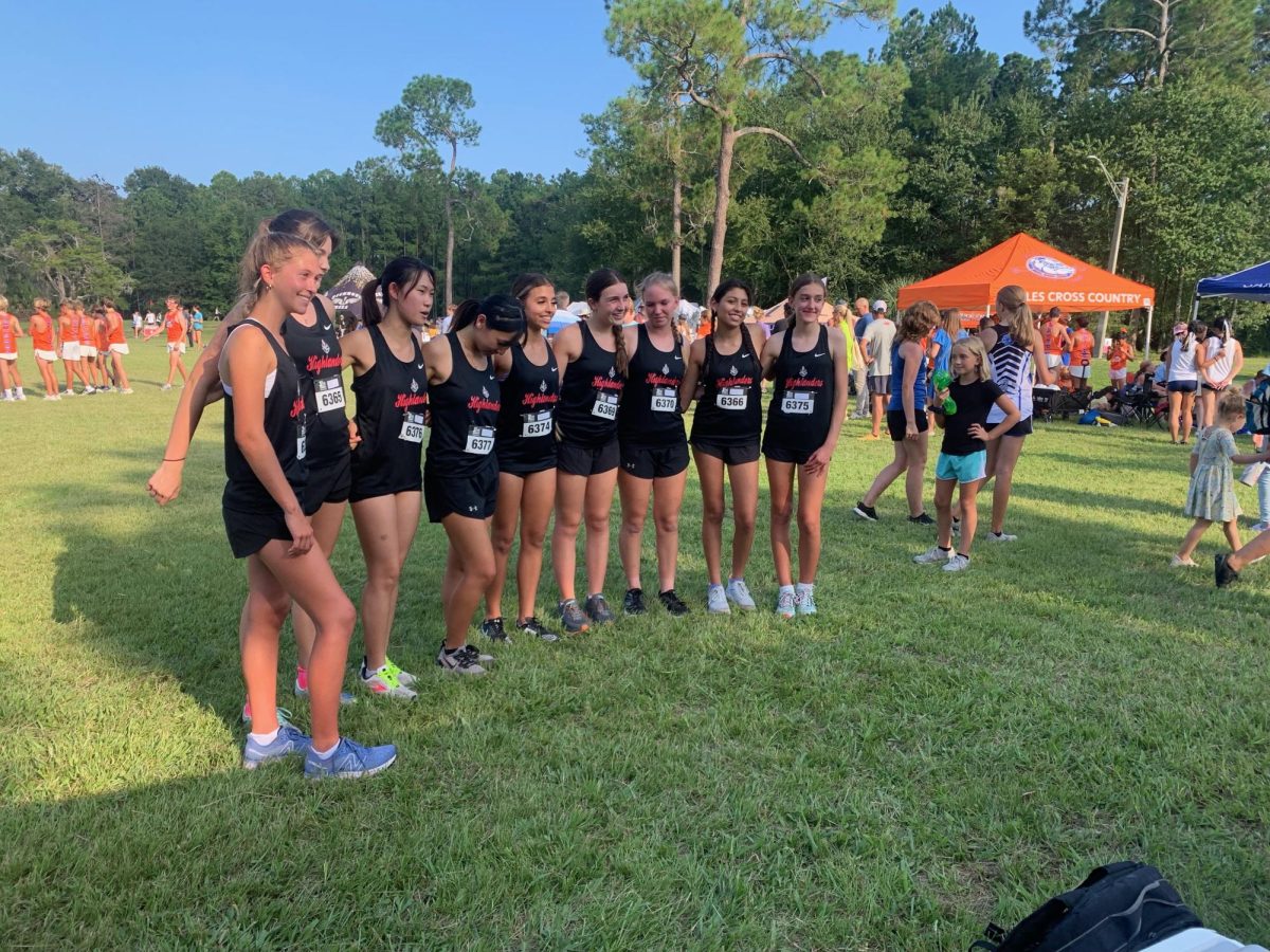 (Above, left to right) Part of the Lake Highland Varsity Girls’ Cross Country team: Sadie D’Andrea, Kate Buckley, Frances Yong, Serena Young, Sofia Tenghoff, Simoni Kyriakou, Emma Larson, Kolbe Madden, and Annabella Tomasic. They are about to begin their race at the Cecil Field Classic in Jacksonville, Florida. Behind them are the tents of the other cross country teams at the meet. The Varsity race began at 6:15, and the Elite race began at 7:15.