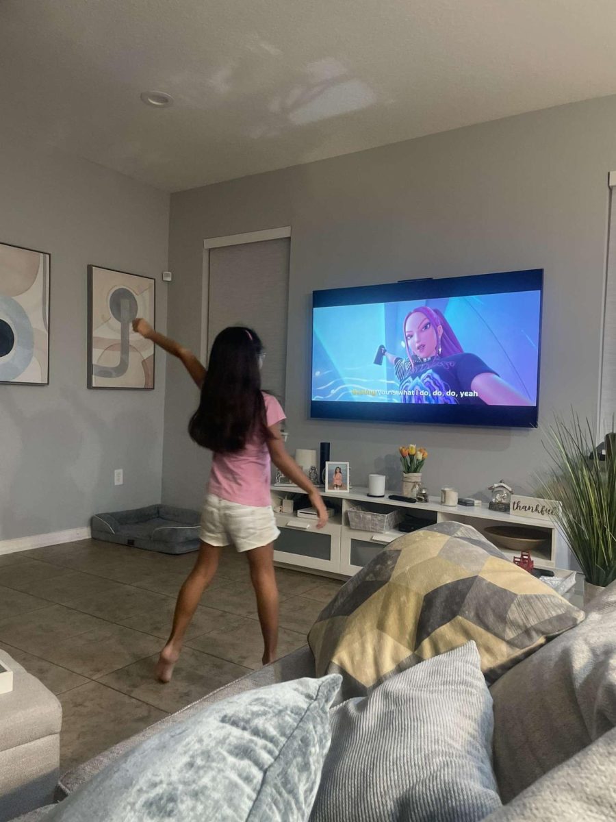 (Above) Mikayla Sanchez, age 7, is one of the many children lured into the world of K-pop through the catchy songs and dances of K-Pop Demon Hunters. Above, Mikayla is seen watching the film in her living room, while also imitating Huntrix, the girl band. Her mom states that everyday after school, she demands practice time to master the choreography of  “Golden,” the film's most popular song.