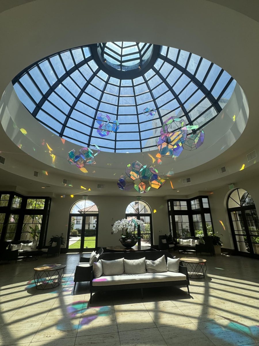(Above) Cloud Cities by Tomás Saraceno floats above, quietly glowing and shifting reflections of light as viewers walk by. Something about the size of the art piece is magnetic and leaves the viewers in awe. When viewers walk into The Alfond Inn they could see in the distance the small atrium projecting the light of the art throughout the room. This makes everyone in the room feel like part of the center-piece. As a viewer standing under the art piece, it is astonishing to see the colors being projected not only on the walls but also on the people viewing the
art piece